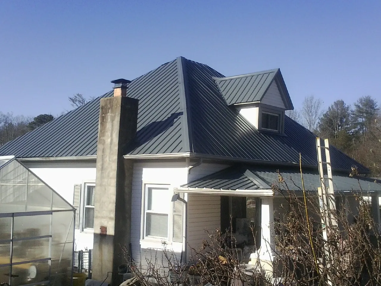 Dark blue standing seam metal roof on a white farmhouse with dormer — Slate & Tile Roof Repair by Roofing Brothers in Butte