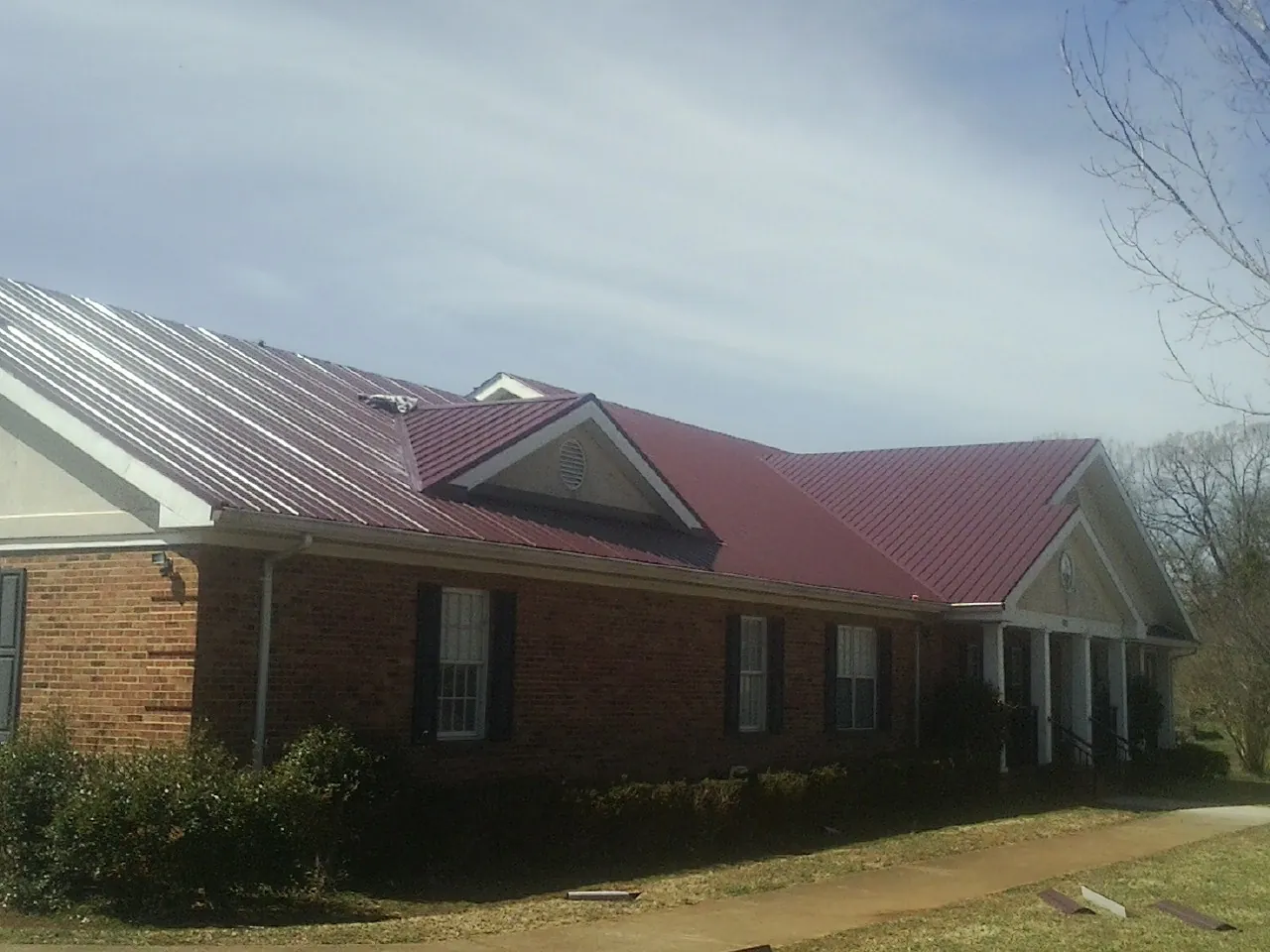 Red metal roof with gabled entries on a long brick building, from a Hail Damage Roof Repair job in Butte