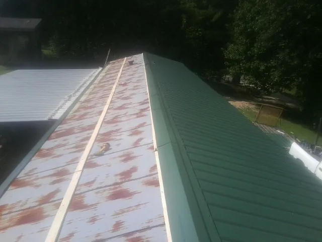 Old rusted panels beside newly installed green metal roofing — Wind Damage Roof Repair by Roofing Brothers in Butte