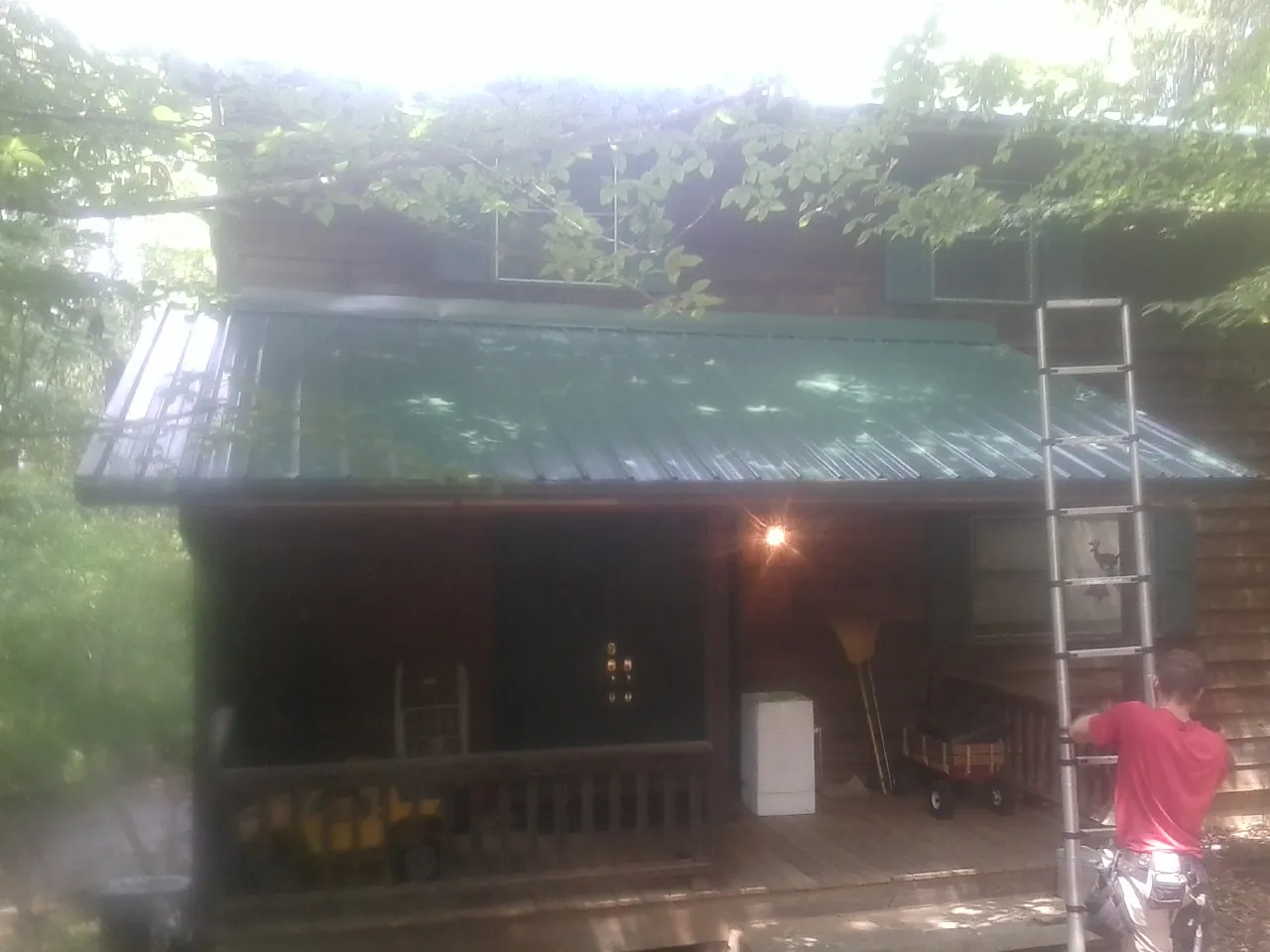 Worker on a ladder at the green porch roof of a wooded cabin in Butte