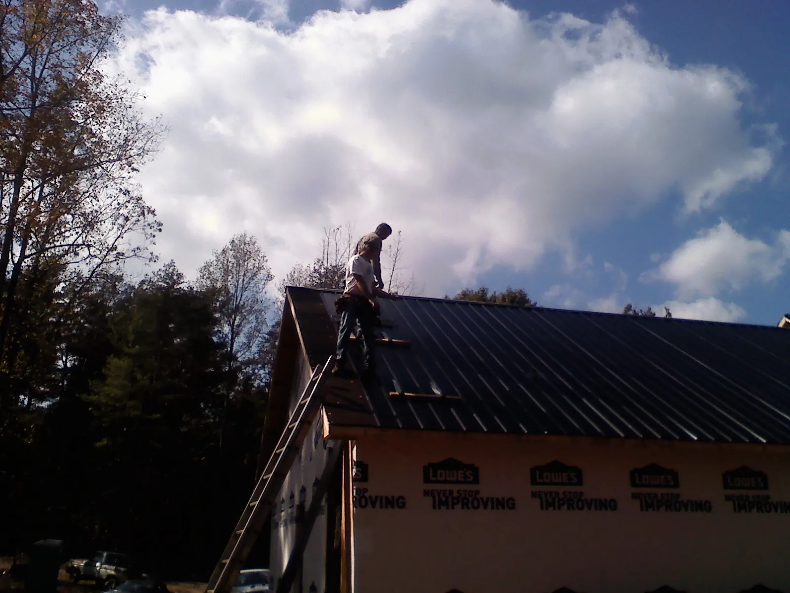 Roofer fastening dark metal panels high against a cloudy sky, from a Roof Inspection job in Butte