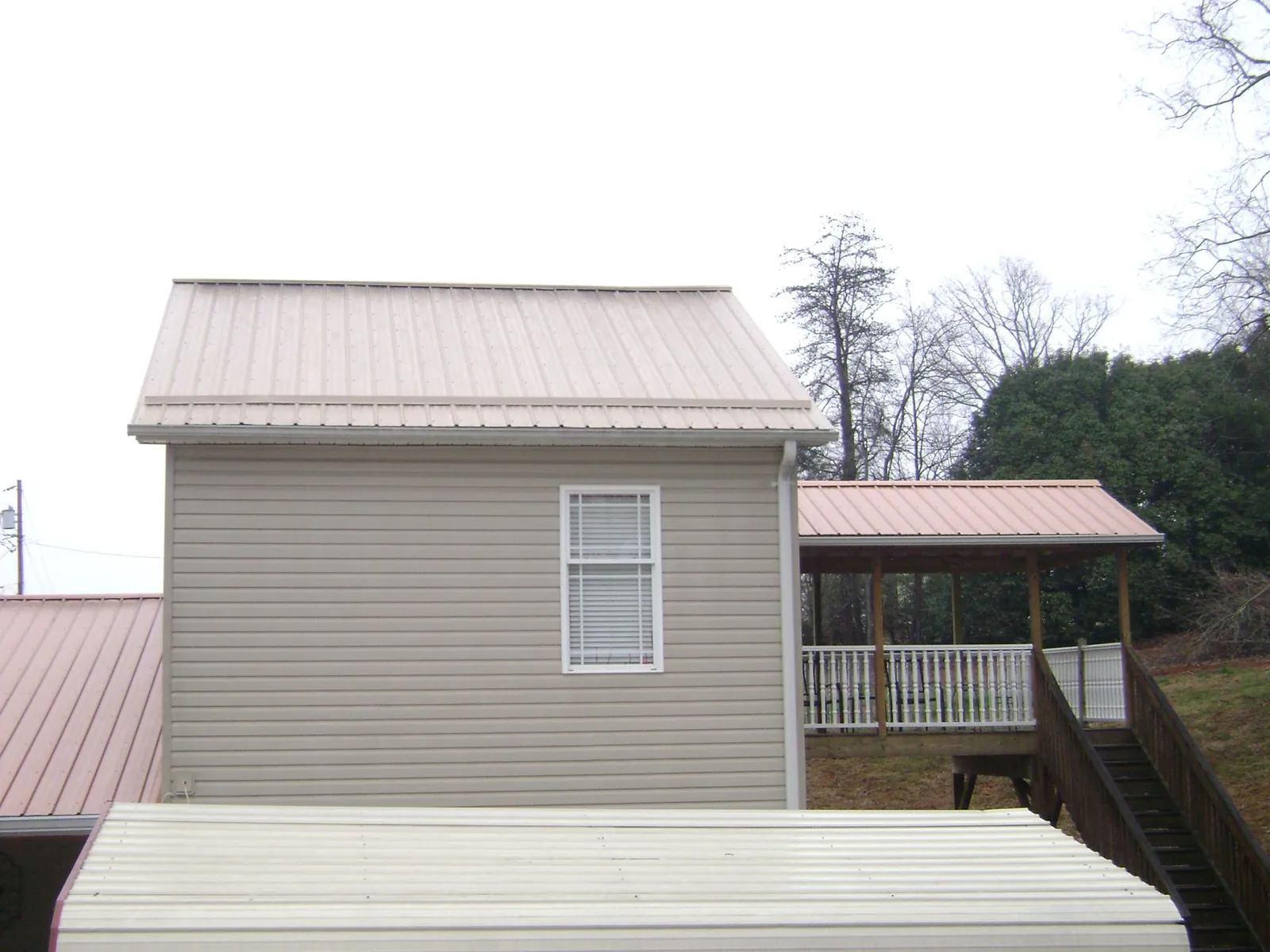Tan metal roofs on a two story addition and attached porch, from a Roof Replacement job in Butte